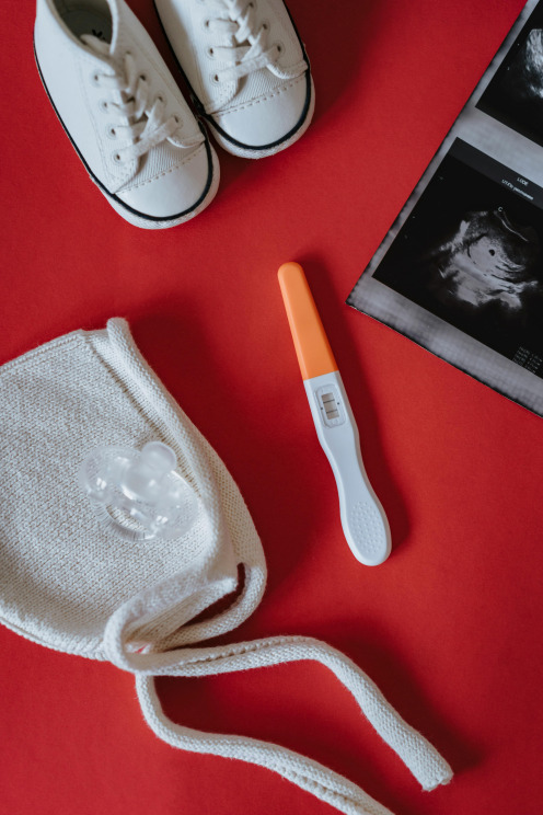 Baby shoes, beanie, ultrasound photos and pregnancy test with positive result